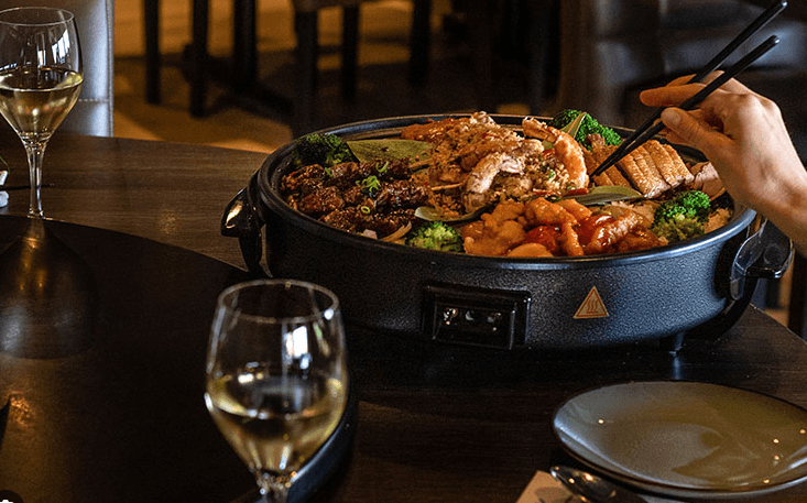 Horeca: gedeelde schotel met Aziatische gerechten, geglazuurd vlees en gamba’s op een gedekte tafel in een restaurant.